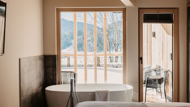 Un baño moderno con bañera, ducha y un amplio ventanal con vistas a un paisaje nevado.