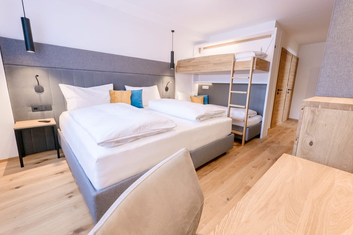 A modern hotel room with a bunk bed, a bedside table, a chair, and a wooden desk.