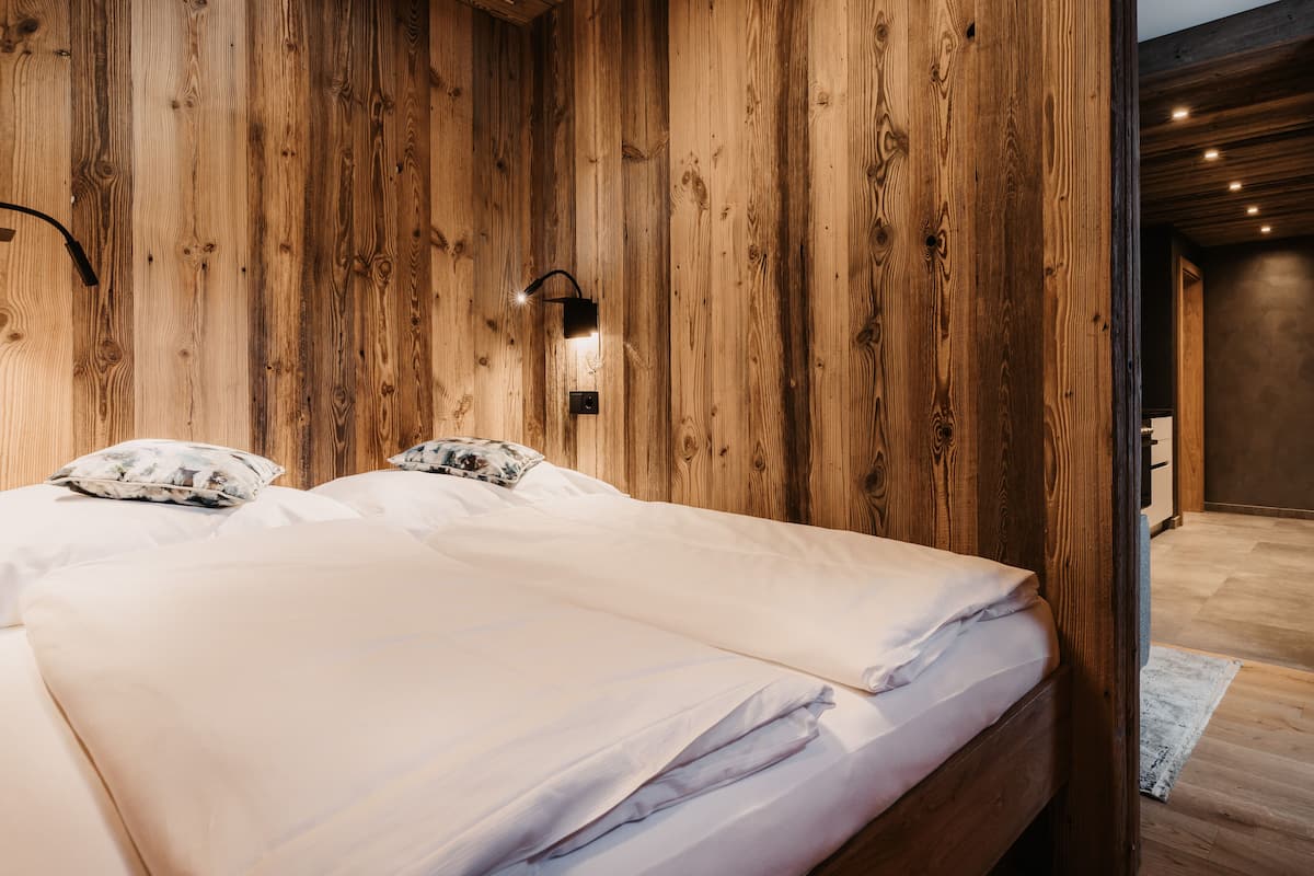 A bedroom with a wooden wall panel design, a bed with white linens, and a wall-mounted light fixture.