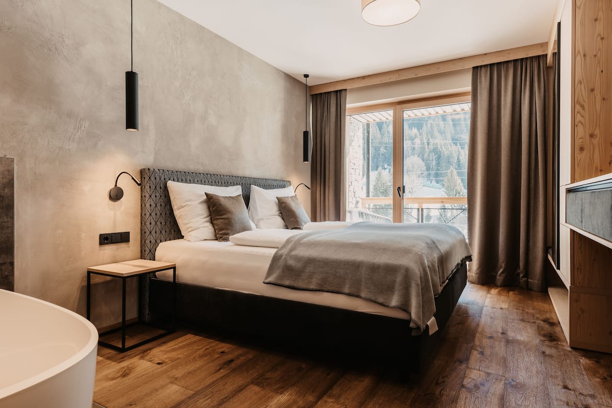 A modern bedroom with a large bed, a bedside table, a wall-mounted light, and a view of a snowy landscape through a window.