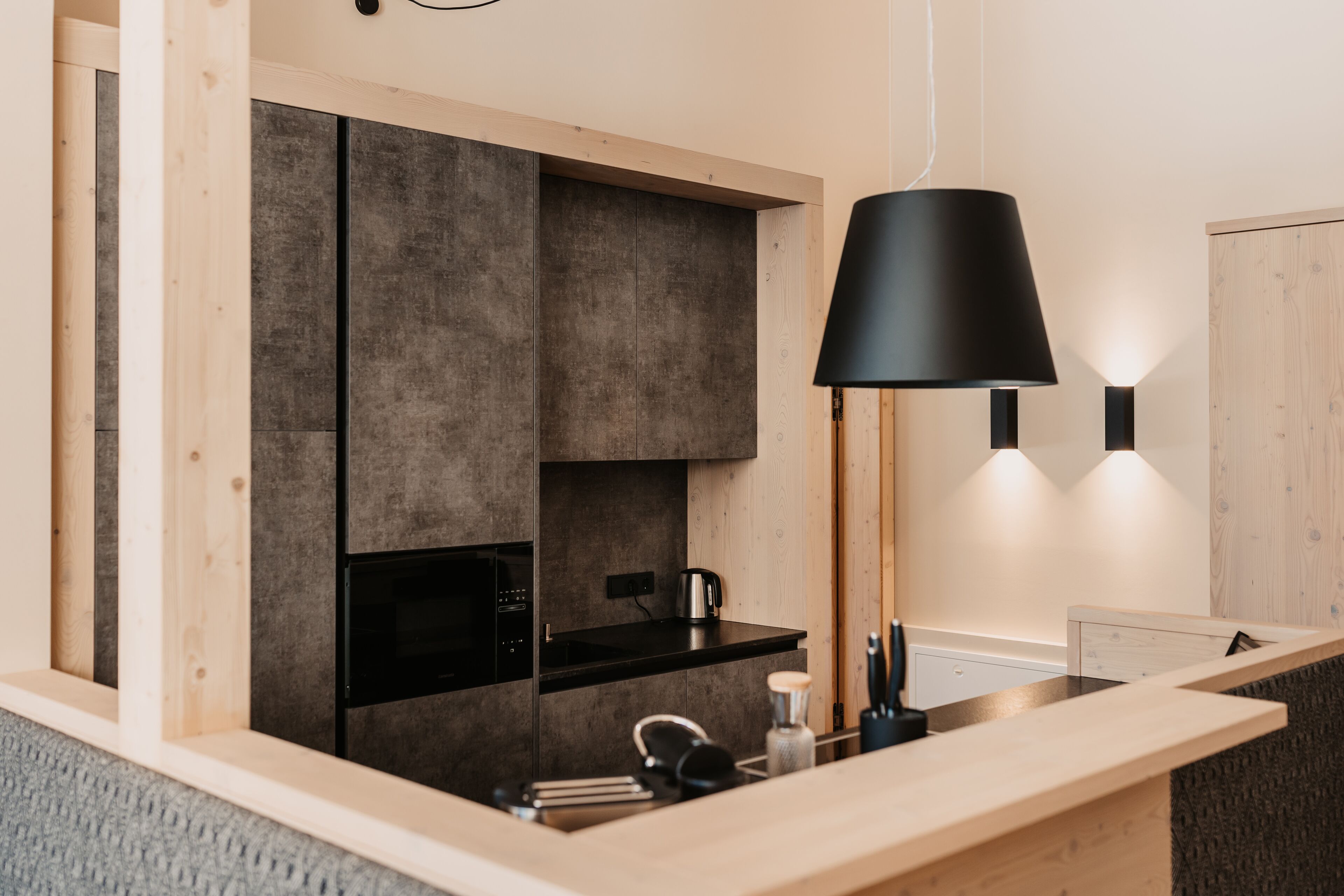 A modern kitchen with a black countertop, a built-in oven, and a hanging black pendant light.