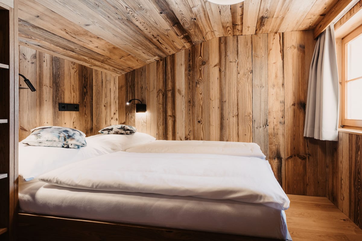 A wooden room with a bed, a wall-mounted light, and a window with curtains.