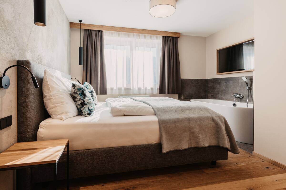 A modern bedroom with a bed, bedside table, and a large window with curtains.