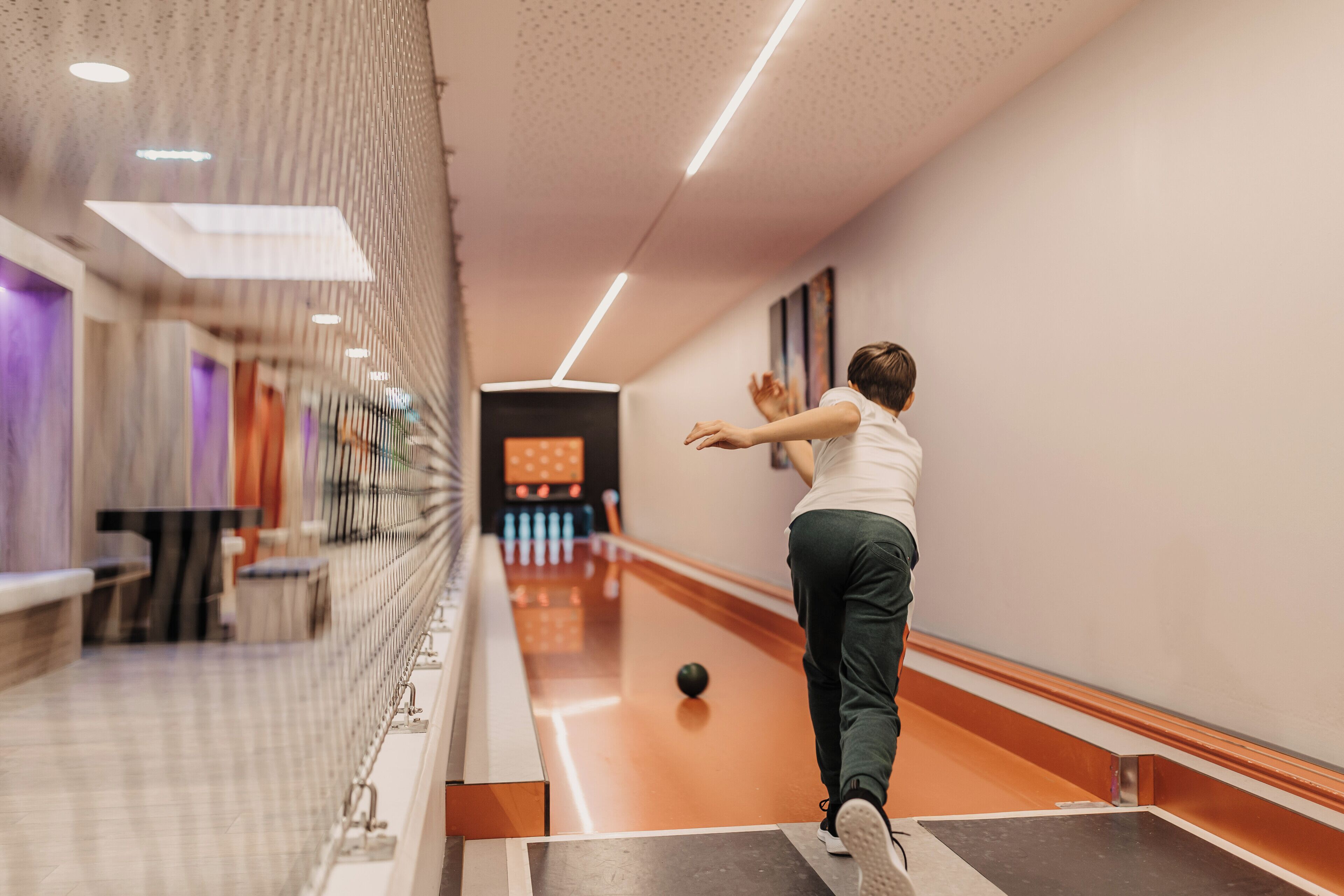 Una bolera con una persona lanzando bolos, una bola de bolos y una máquina de colocación de bolos.