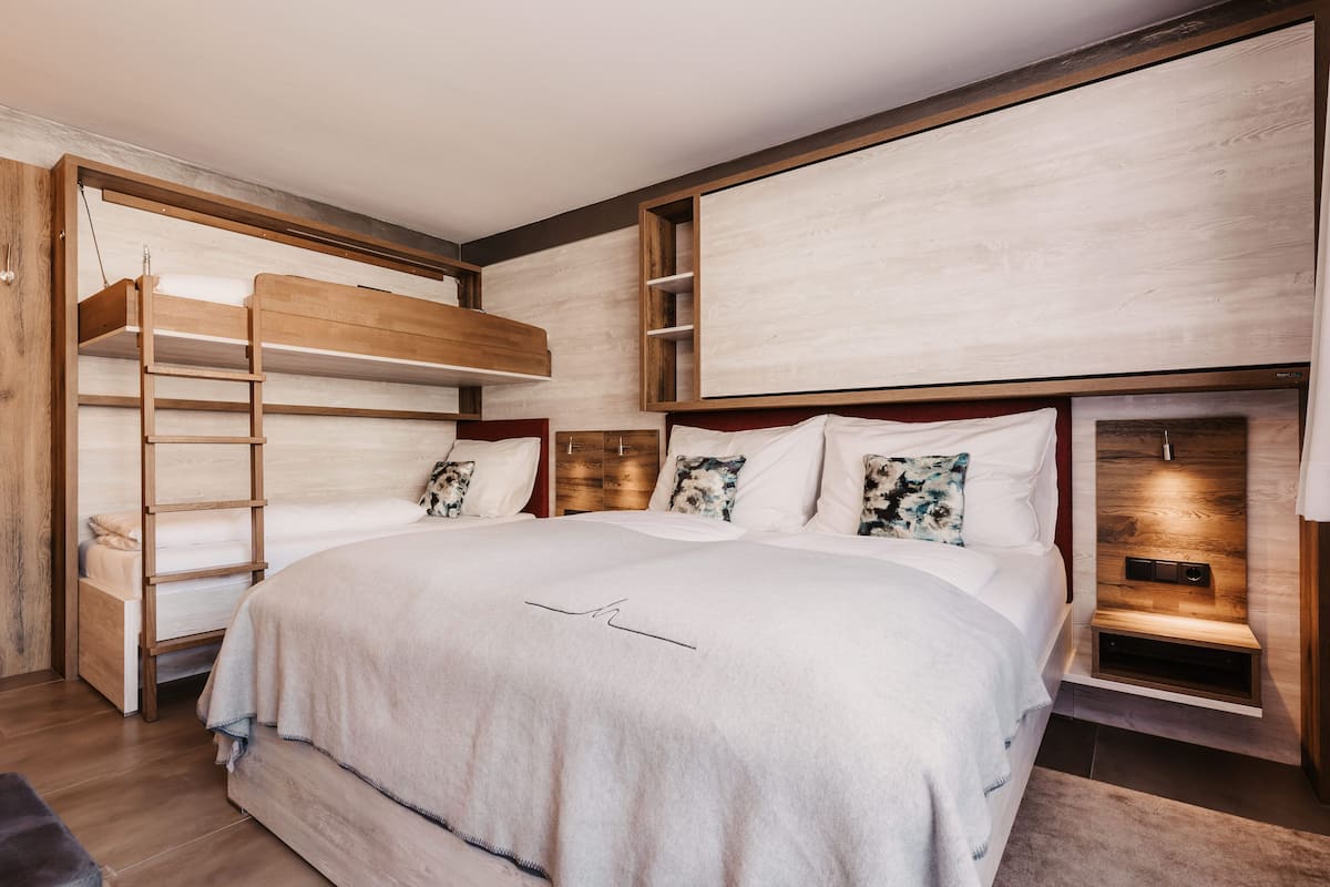 A bedroom with a bunk bed, a wooden ladder, a bedside table, and a headboard with built-in lighting.