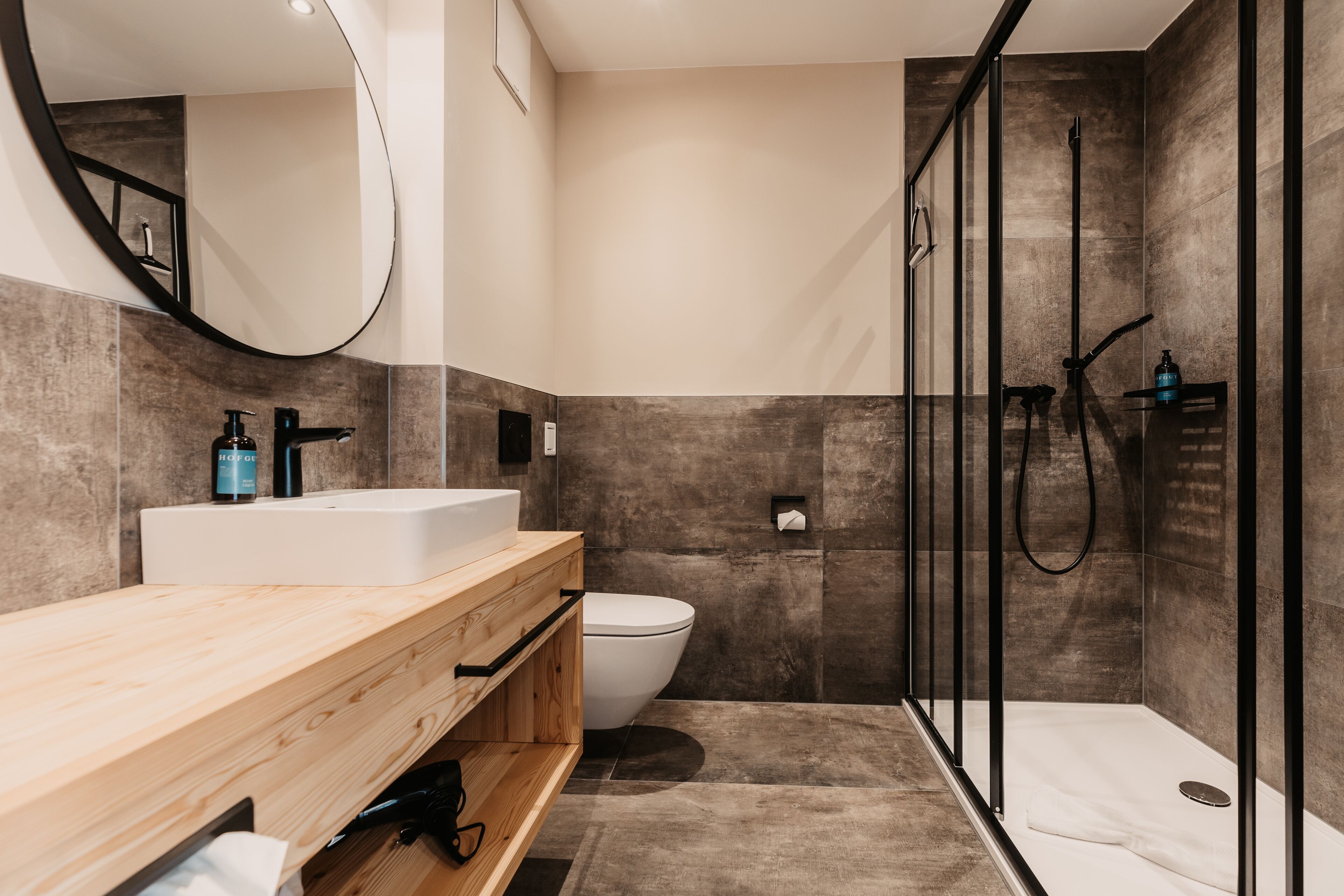 A modern bathroom with a wooden vanity, a white sink, a toilet, and a glass-enclosed shower area.