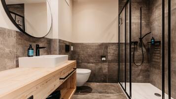 A modern bathroom with a wooden vanity, a white sink, a toilet, and a glass-enclosed shower area.