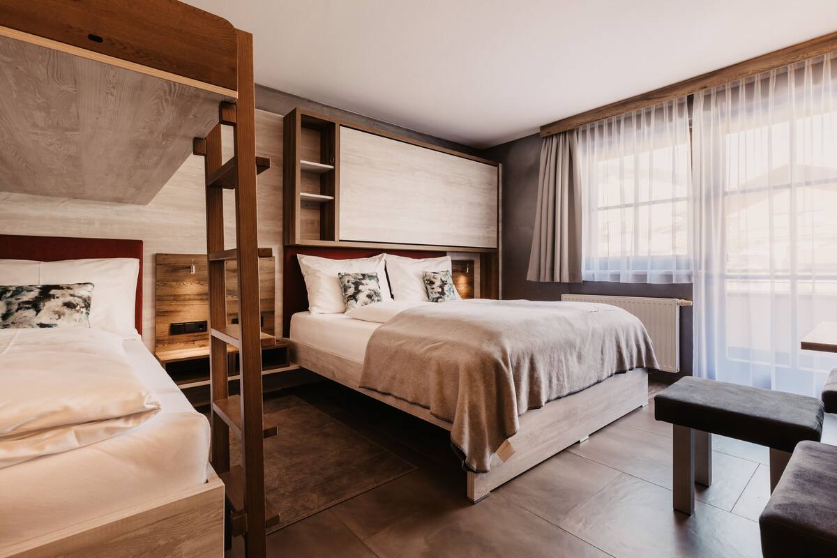 A modern hotel room with a bunk bed, a desk, and a large window with sheer curtains.