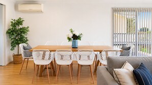 A dining area with a wooden table and white wireframe chairs, a potted plant, and a grey sofa with cushions. - Seaview Cowes by Ready Set Stay (Cowes)
