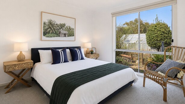 A bedroom with a large bed, two bedside tables, a window with a view of greenery, and a chair. - Seaview Cowes by Ready Set Stay (Cowes)