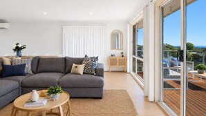 A modern living room with a grey sectional sofa, a small wooden coffee table, and a large sliding glass door leading to an outdoor balcony. - Seaview Cowes by Ready Set Stay (Cowes)