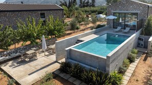 Uma área moderna de piscina ao ar livre, com paredes de pedra, um espaço de estar com mesas e cadeiras, e vista para a paisagem circundante.