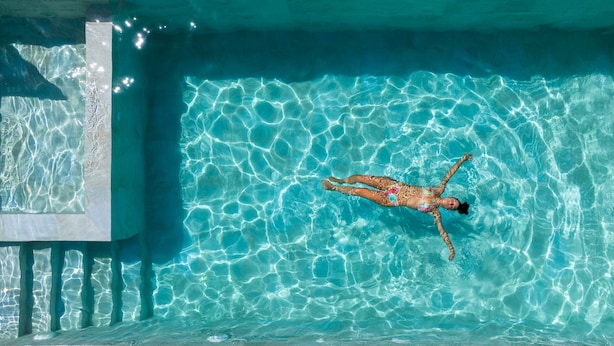 Una persona flotando en una piscina azul cristalina, con ondulaciones en el agua y borde de azulejos.