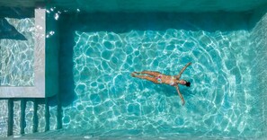 Une personne flotte dans une piscine à l’eau claire et bleue, où l’on peut voir de légères ondulations à la surface et un bord de piscine carrelé.