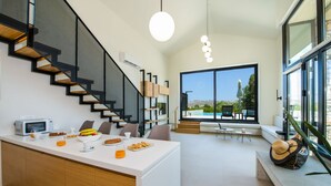 Una cocina moderna con una isla central, una escalera con barandas negras y un área de comedor con vista al exterior.
