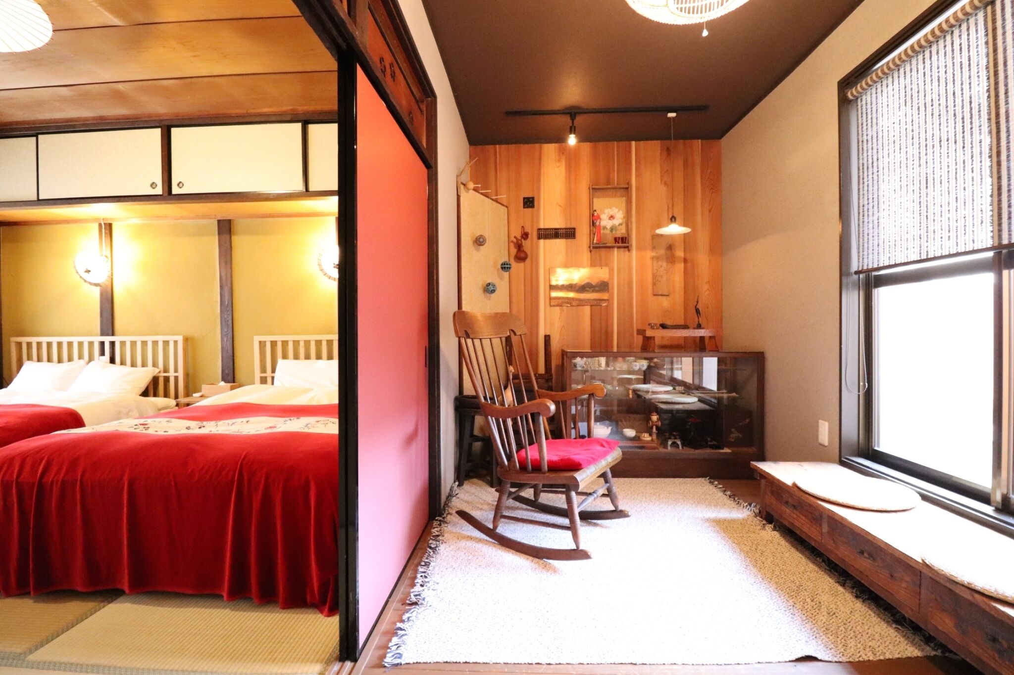 A room with two beds, a rocking chair, a wooden cabinet, and a large window.