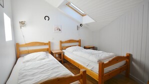 Huoneessa on kaksi puista sänkyä, pieni pöytä ja seinään kiinnitetty valaisin.