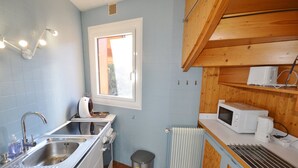 Pieni, käytännöllinen keittiö, jossa on pesuallas, liesi, mikroaaltouuni ja ikkuna.