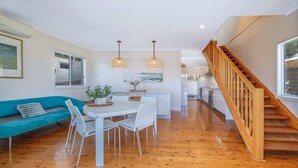 A modern kitchen with white cabinets, a wooden staircase, and a dining area with a white table and chairs. - Pretty Beach Bay Vista by HolidayCo. (PRETTY BEACH)