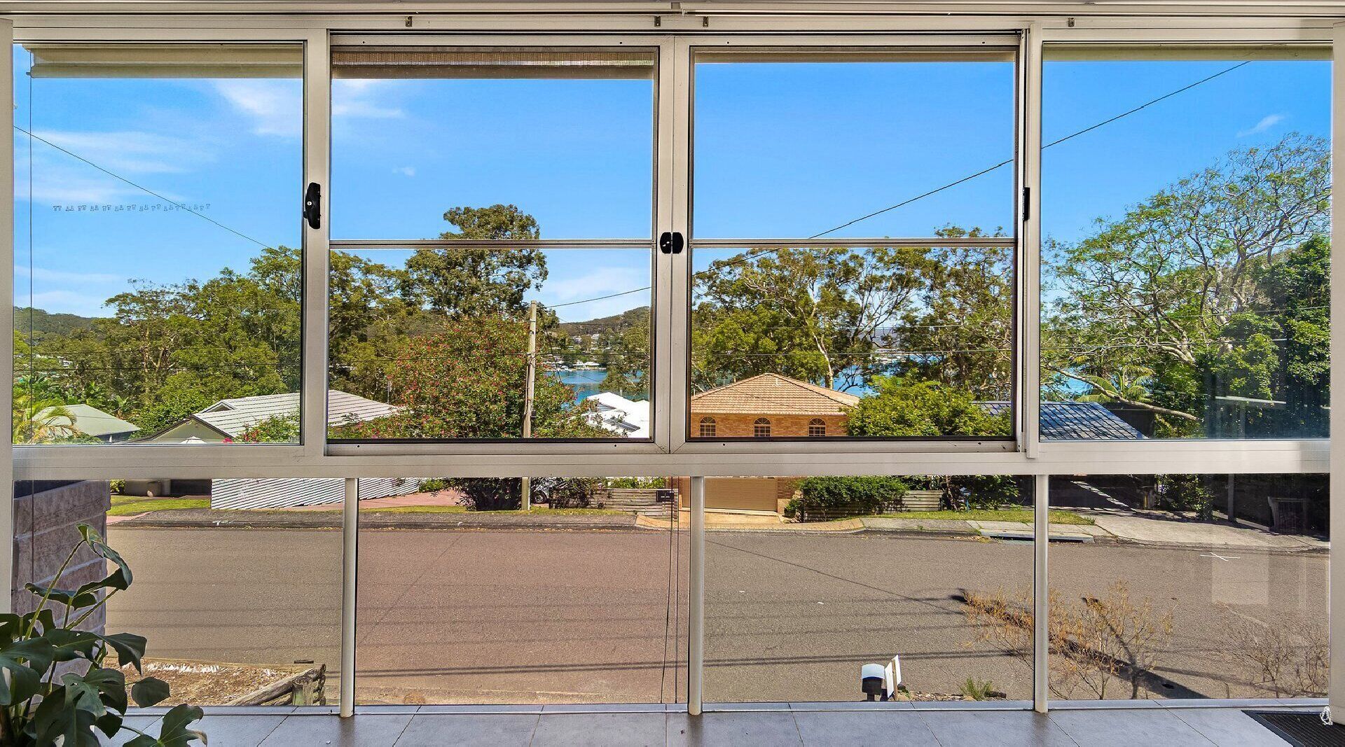 Une vue à travers une grande fenêtre à carreaux multiples, donnant sur un parking et une zone résidentielle avec des maisons et des arbres.