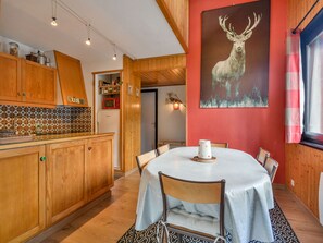 Un coin repas avec une table ronde, des meubles en bois et un mur rouge orné d’un tableau représentant un cerf.