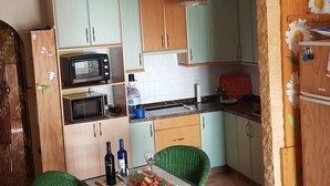 Cozinha compacta com armários verdes, micro-ondas, pia e área de refeições com duas cadeiras verdes.