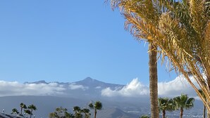 Um copo de bebida vermelha num terraço com vista para uma montanha e edifícios brancos.