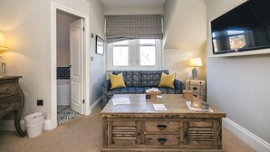 A room with a wooden coffee table, a blue sofa with yellow cushions, a television on the wall, and a patterned window valance. - The Whittling House (Alnwick)