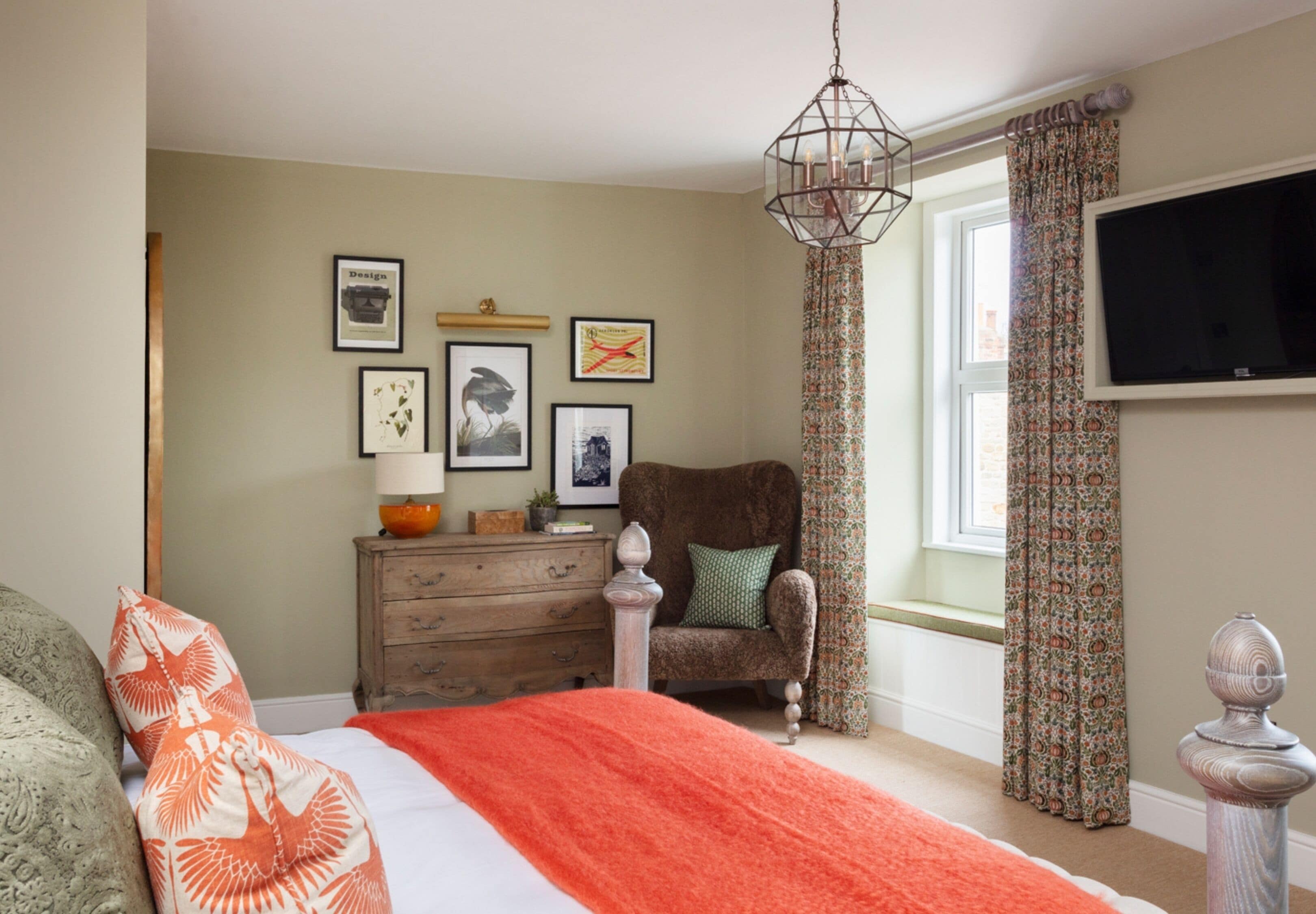 A bedroom with a bed, dresser, chair, and a TV mounted on the wall.