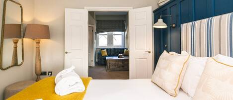 Habitación de hotel con cama, una manta amarilla, un espejo y vista a la habitación contigua.