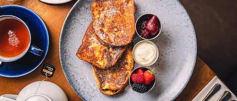 A plate of French toast with berries and whipped cream, a cup of tea, and a teapot on a wooden table.