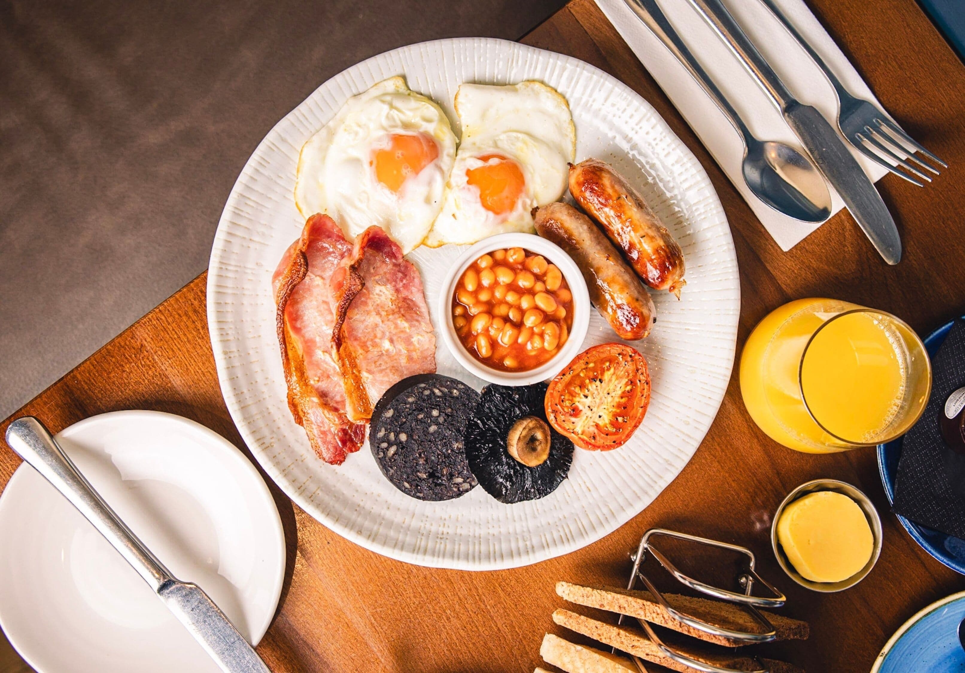 Une assiette de petit-déjeuner comprenant des œufs, des saucisses, du bacon, des haricots, du boudin noir et des toasts.