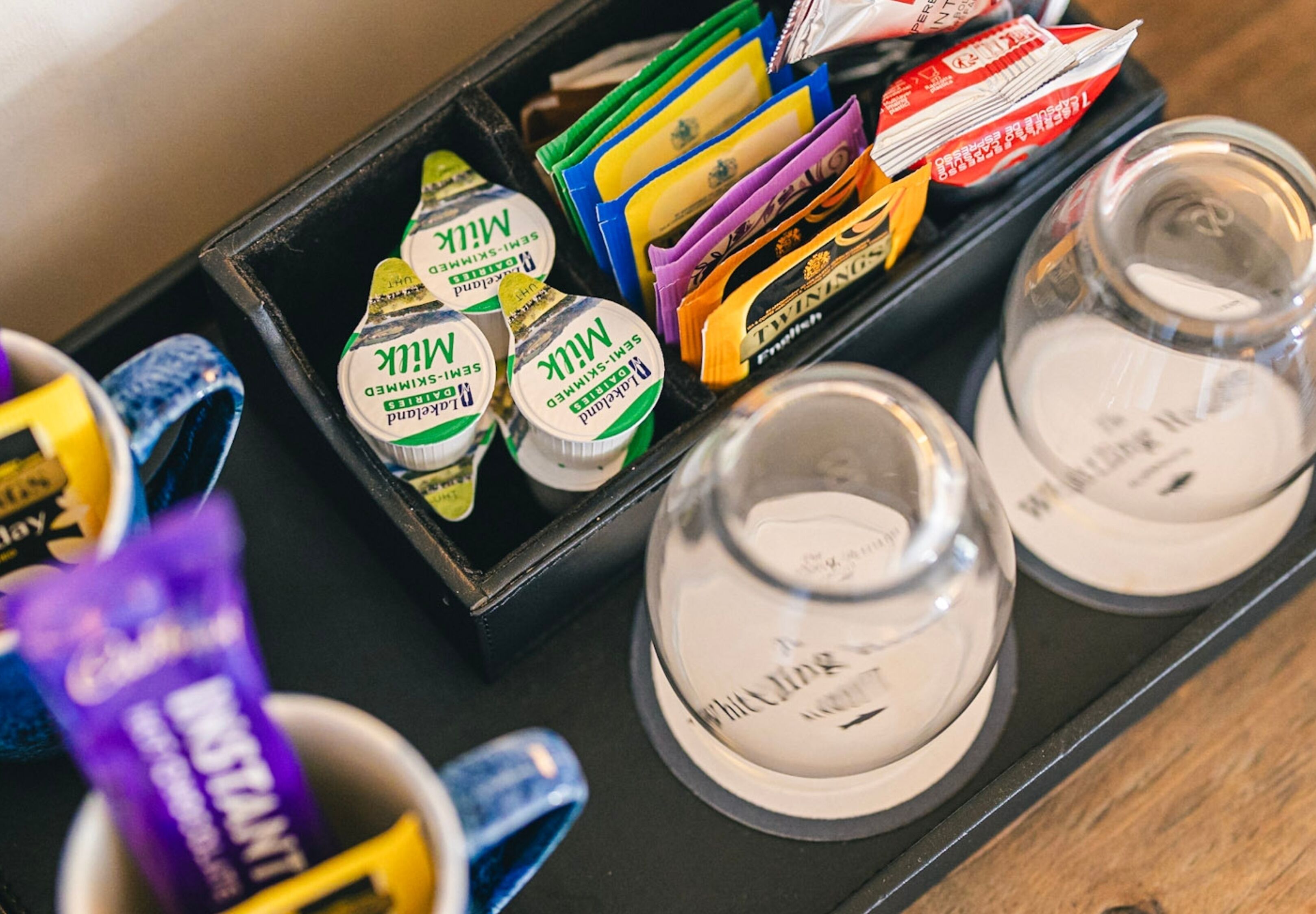 A tray with various packaged items, including milk and instant coffee, and two clear glasses.