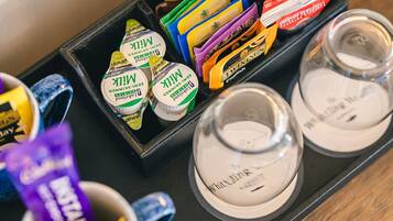 A tray with various packaged items, including milk and instant coffee, and two clear glasses.