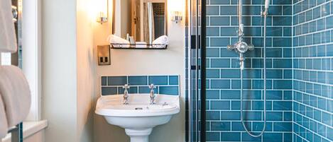 A bathroom with a white pedestal sink, a mirror with wall sconces, and a shower with blue-tiled walls.