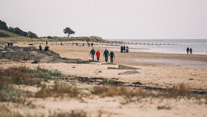 A beach with people walking, a sandy area, and a wooden pier in the distance. - The Whittling House (Alnwick)