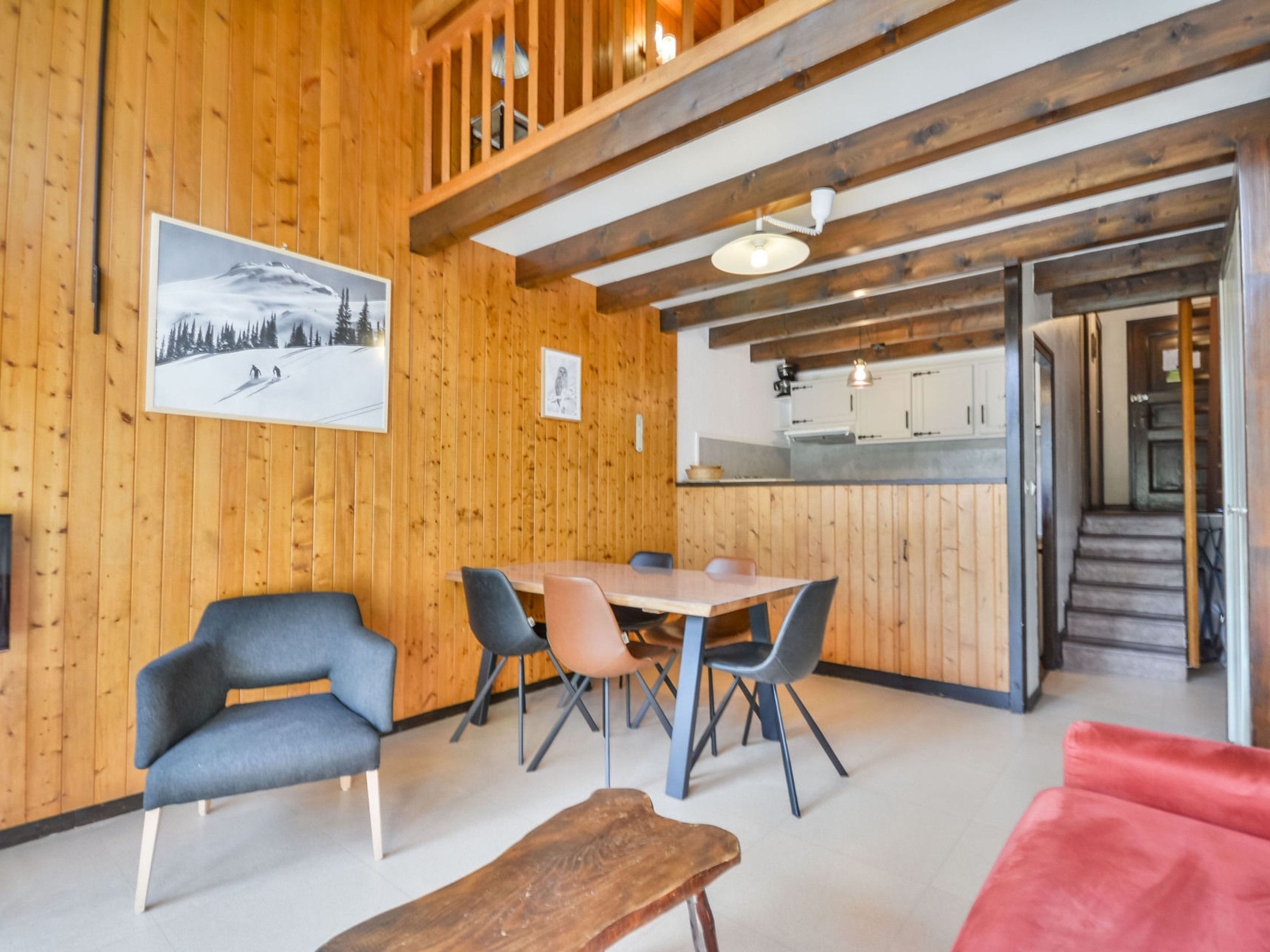 Een houten interieur met een eethoek, stoelen, een bank en een trap naar een andere kamer.