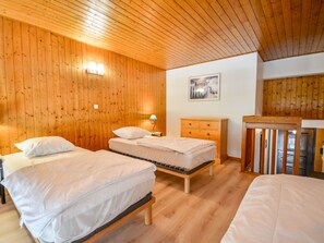 Ein Zimmer mit zwei Betten, Holzwänden, einer Holzbalkendecke, einem Nachttisch mit Lampe und einer Holzkommode.