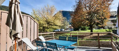 An outdoor patio with a table and chairs, a covered seating area, and a view of a tree-lined street and hills in the background.