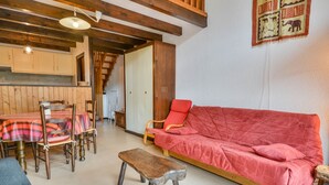 A cozy living room with a wooden bench, a red sofa, and a dining area with striped tablecloths and wooden chairs. - Duplex Studio 5 pers. in Central Morzine, near Slopes (Morzine)