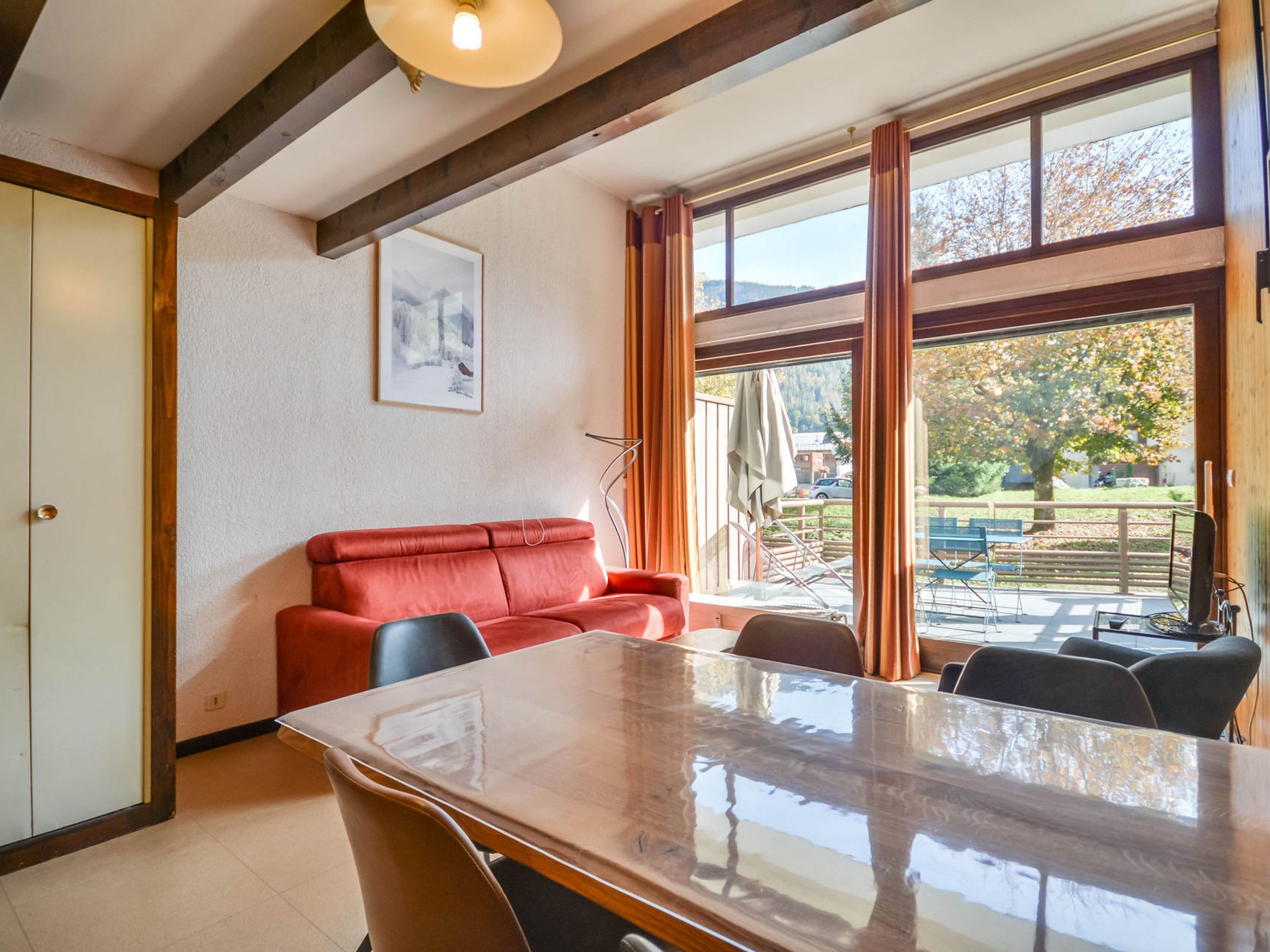 A dining area with a table and chairs, a red sofa, and a window with a view of the outdoors.