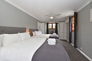 A hotel room with two beds, a ceiling fan, a window with curtains, and a door.
