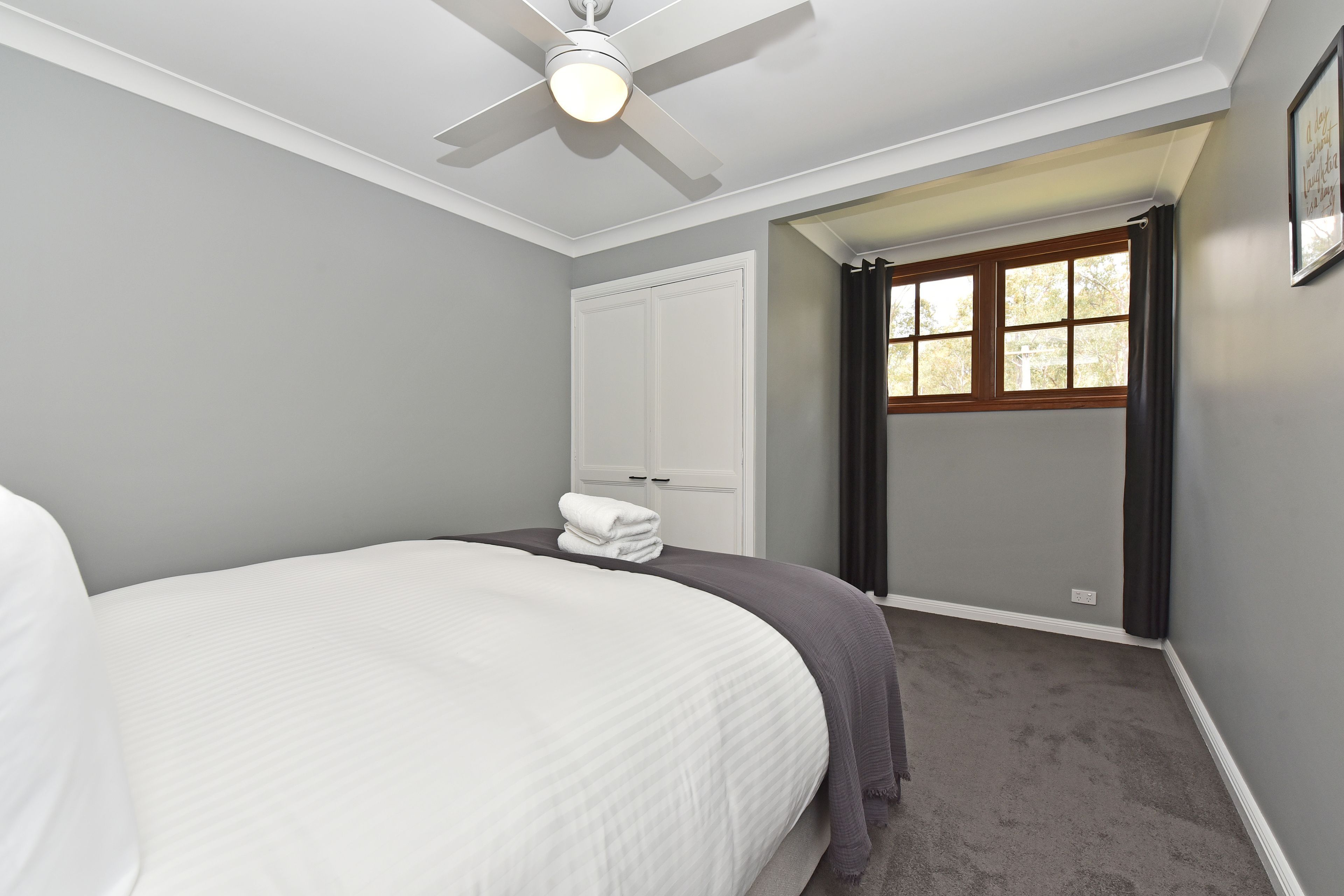 A bedroom with a bed, a ceiling fan, a window with curtains, and a door.