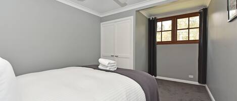 A bedroom with a bed, a ceiling fan, a window with curtains, and a door.