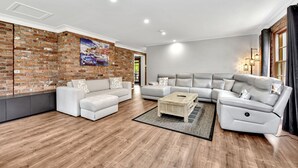Un salon moderne avec un mur en briques, deux canapés, une table basse et une grande fenêtre avec des rideaux.