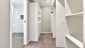Un couloir étroit, avec des étagères blanches de part et d’autre, une porte d’entrée en verre et un sol recouvert de moquette.