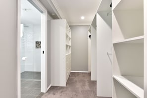 A narrow hallway with white shelving units on both sides, a glass door entrance, and a carpeted floor.