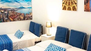 A hotel room with two beds, a nightstand, and a lamp. There are paintings on the wall depicting cityscapes and architecture. - Napoli SottoSopra a Chiaia, Elegant central apartment for groups and families (Napoli)