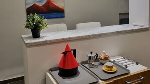 A modern hotel lobby with a marble reception desk, a painting of a volcano, a potted plant, and a coffee station. - Napoli SottoSopra a Chiaia, Elegant central apartment for groups and families (Napoli)