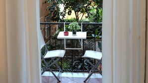 A balcony with a table and chairs, a potted plant, and a view of a tree and building. - Napoli SottoSopra a Chiaia, Elegant central apartment for groups and families (Napoli)